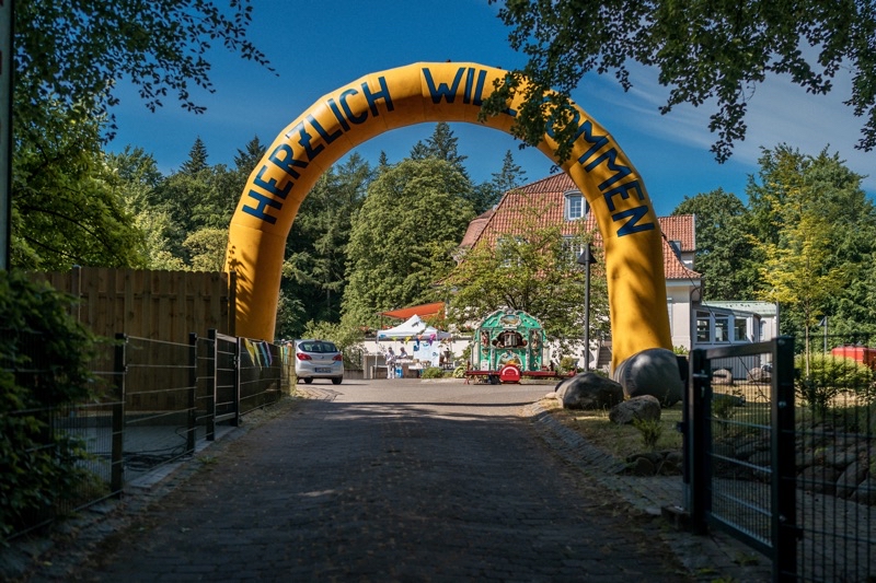 Gelber Bogen mit dem Schriftzug 'Herzlich Willkommen' am Eingang eines Geländes.