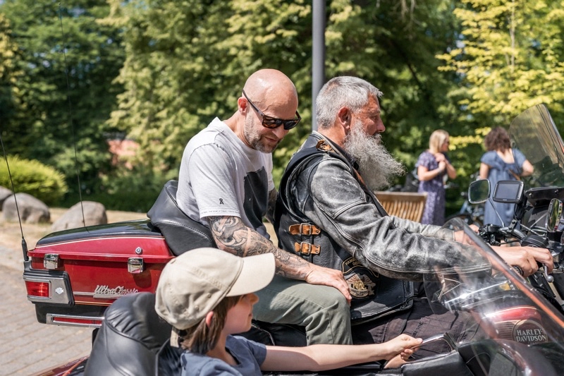 Zwei Männer sitzen auf einem Motorrad, ein Junge im Beiwagen daneben.