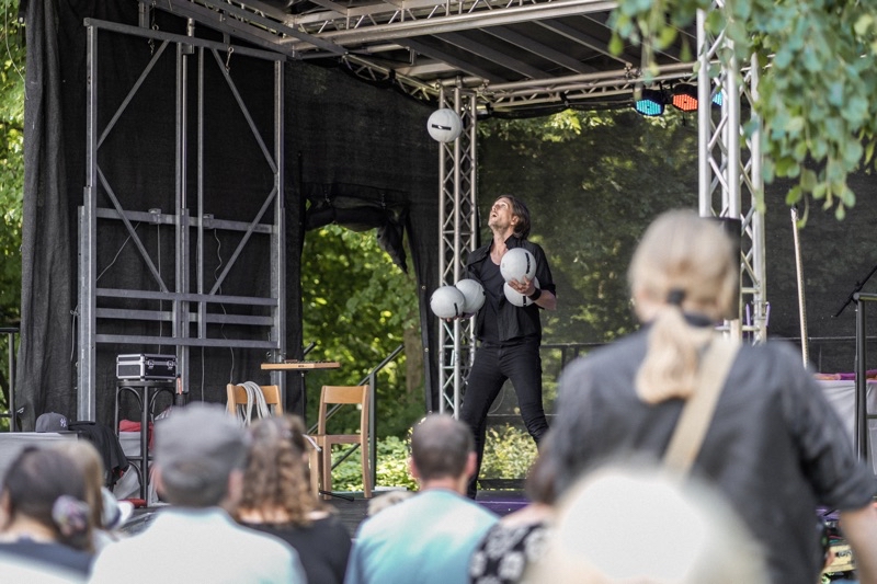 Ein Jongleur, der auf einer Bühne mit mehreren Bällen jongliert, während Zuschauer zuschauen.