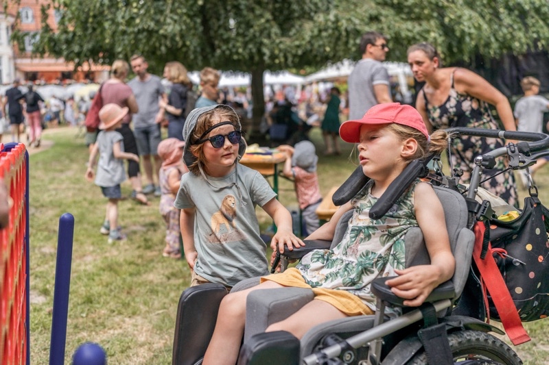 Zwei Kinder auf einem Sommerfest, eines im Rollstuhl und das andere mit Sonnenbrille.