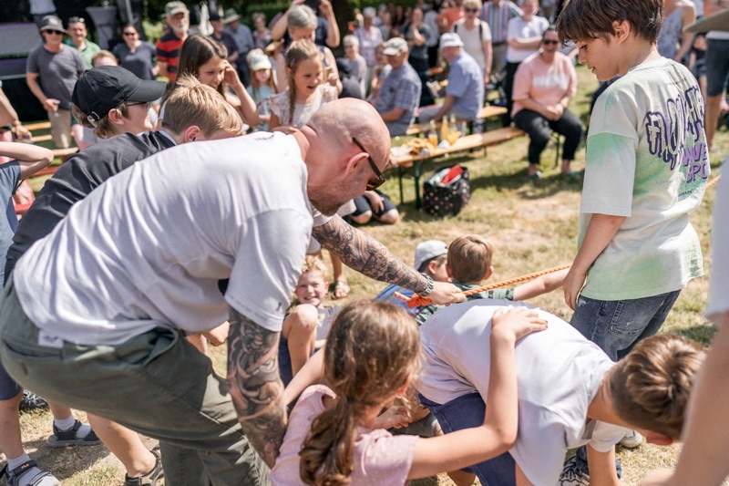 Gruppe von Kindern und Erwachsenen, die an einem Seil ziehen im Freien.