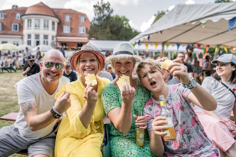 Vier Personen im Freien lächeln und halten gelbe Lose in die Kamera.