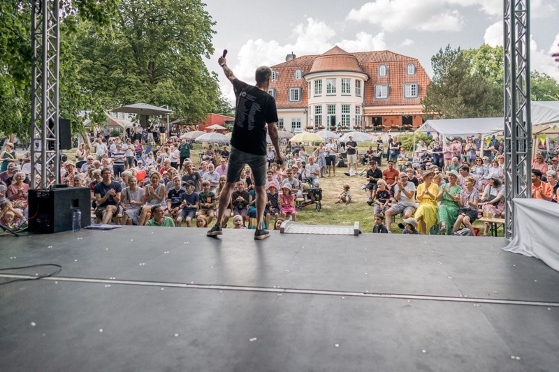 Ein Mann steht auf einer Bühne und spricht zu einem Publikum im Freien.