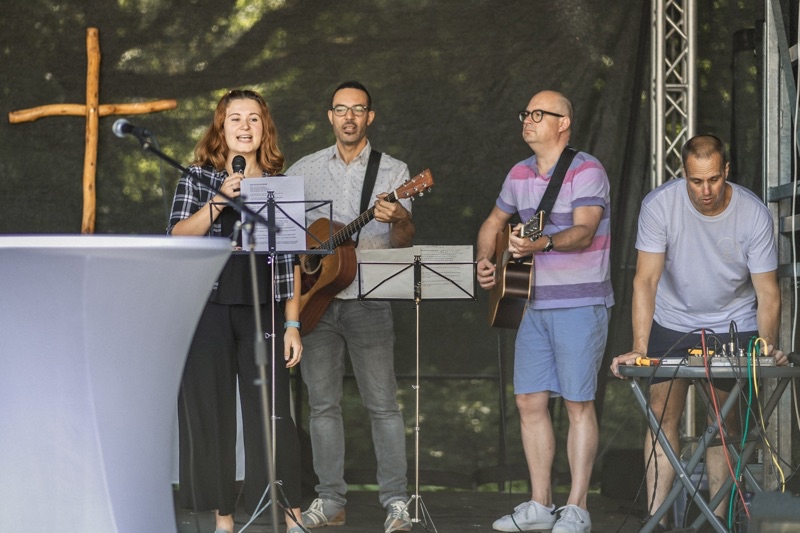 Eine Sängerin und zwei Gitarristen auf einer Bühne, neben ihnen ein Mann am Technikpult.