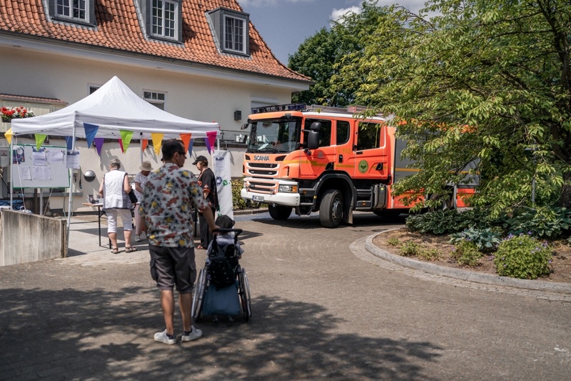 Ein orangefarbenes Feuerwehrfahrzeug steht neben einem Pavillon bei einer Veranstaltung.