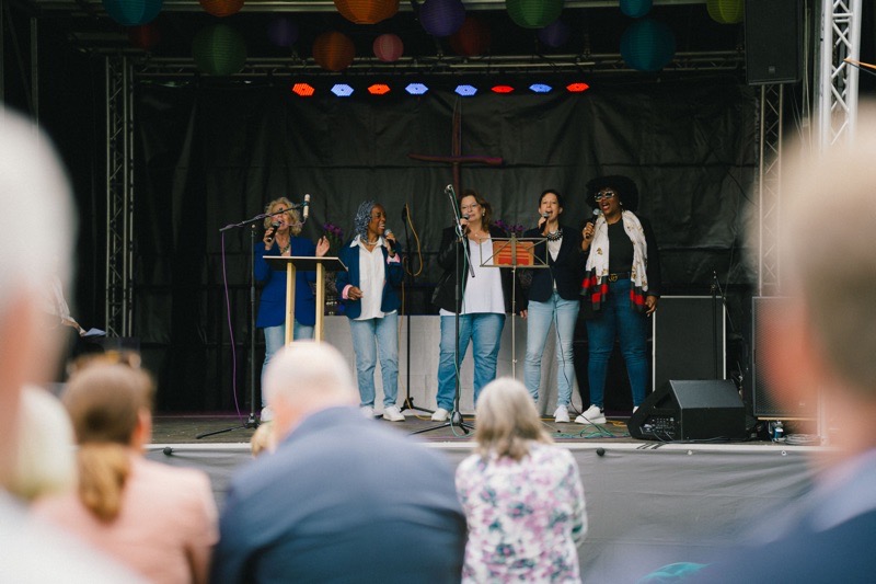 Fünf Sängerinnen stehen auf einer Bühne und singen in ein Mikrofon.