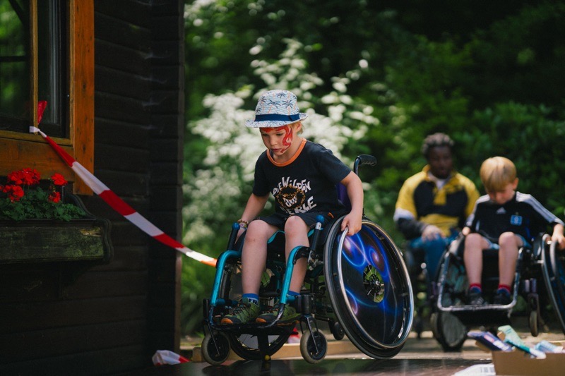 Ein Junge im Rollstuhl fährt über einen Holzsteg.
