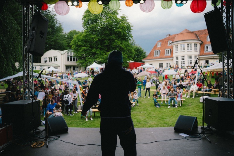 Eine Person spricht auf einer Bühne vor einer Menschenmenge im Freien.