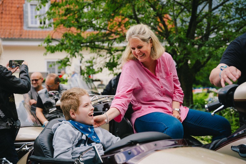 Eine Frau sitzt neben einem Jungen in einem Motorradgespann, beide lächeln und interagieren.