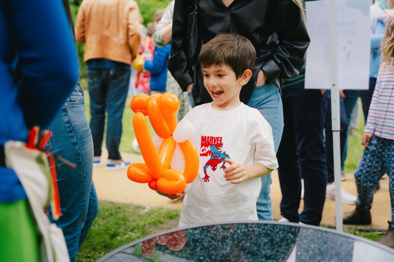 Ein Junge hält eine orangefarbene Luftballonfigur in der Hand und lächelt.
