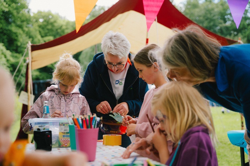 Gruppen von Kindern und Erwachsenen bei einem kreativen Workshop im Freien, umgeben von Bastelmaterialien.