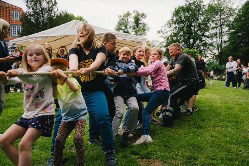Gruppe von Kindern und ein Erwachsener, die an einem Tauziehen teilnehmen.