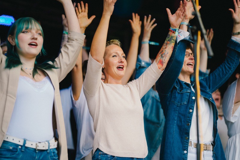 Gruppe von Menschen mit erhobenen Händen, die auf einer Bühne stehen und singen.