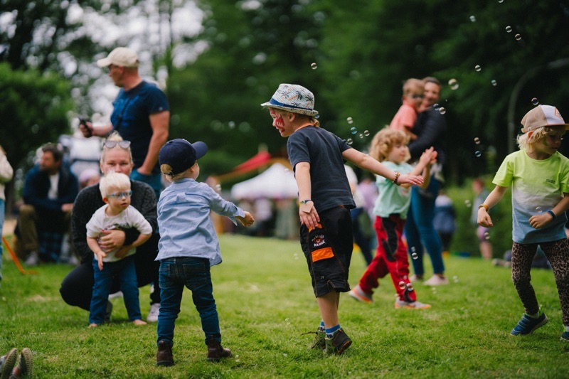 Eine Gruppe von Kindern spielt und läuft auf Rasen während Seifenblasen in der Luft schweben.