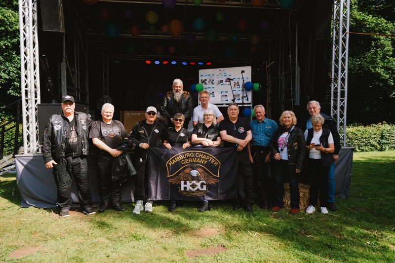 Gruppe von Motorradfahrern des Hamburg Chapter steht vor einer Bühne im Freien.
