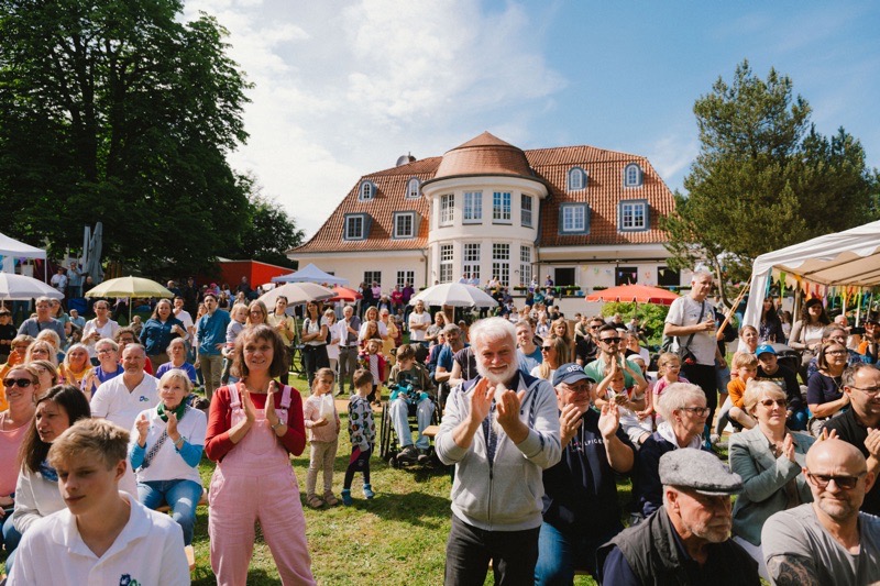 Eine große Menschenmenge applaudiert während einer Veranstaltung im Freien vor einem Gebäude.