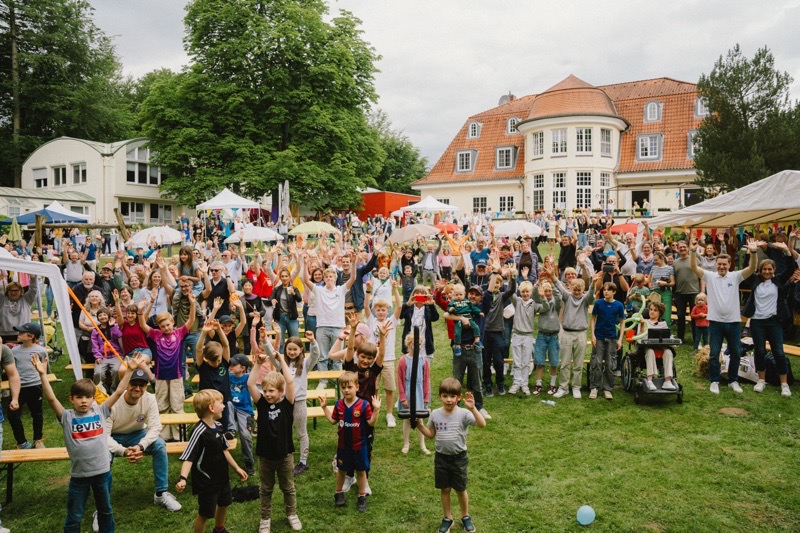 Eine große Gruppe von Menschen, darunter viele Kinder, die bei einem Sommerfest im Freien jubeln.