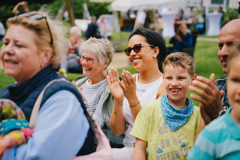 Gruppe von Menschen, die lächeln und applaudieren, darunter Erwachsene und Kinder.