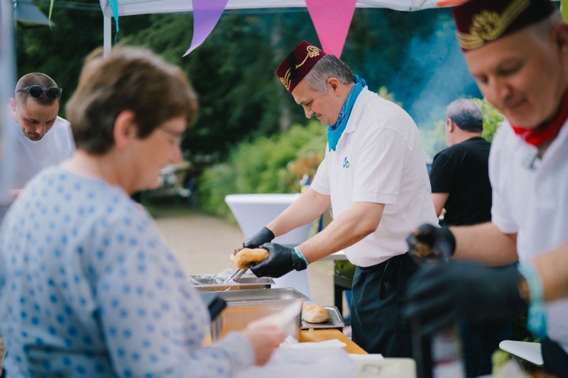 Männer in weißen T-Shirts und mit roten Kopfbedeckungen bereiten Speisen an einem Buffet vor.
