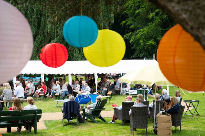 Bunte Lampions hängen über einer Gruppe von Menschen, die in einem Garten sitzen.