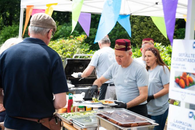 Mehrere Personen in grauen T-Shirts servieren Essen an einem Stand während eines Sommerfestes.