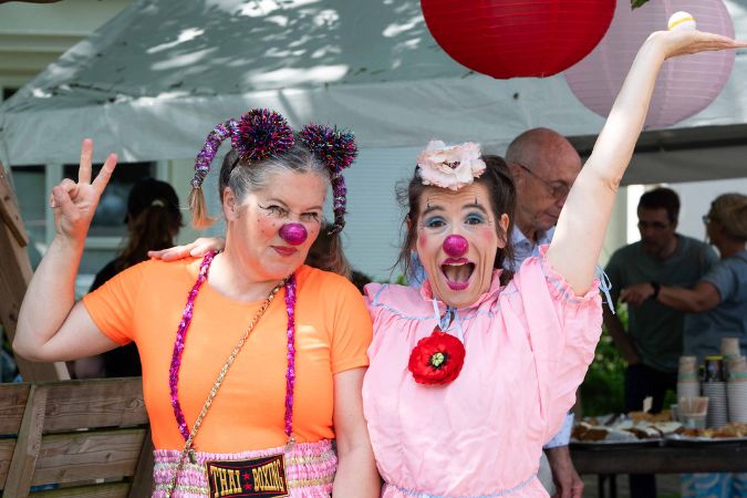Zwei Clowns mit bunten Kostümen und Schminke stehen zusammen und posieren fröhlich für die Kamera.