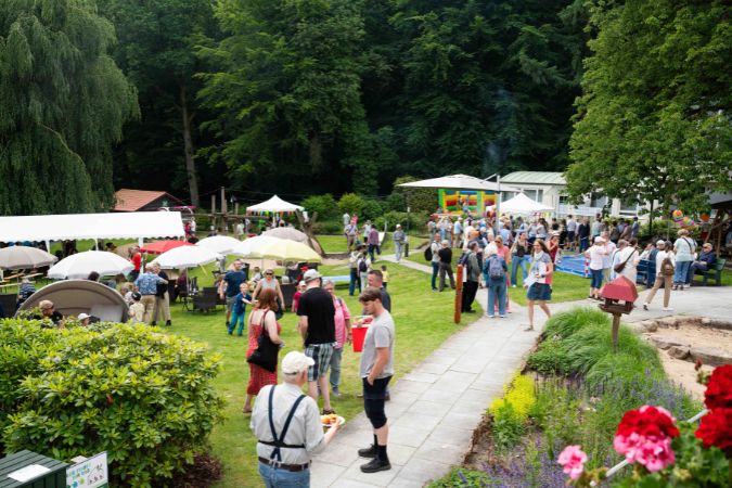 Menschenmenge bei einem Sommerfest im Freien mit Ständen und Aktivitäten.