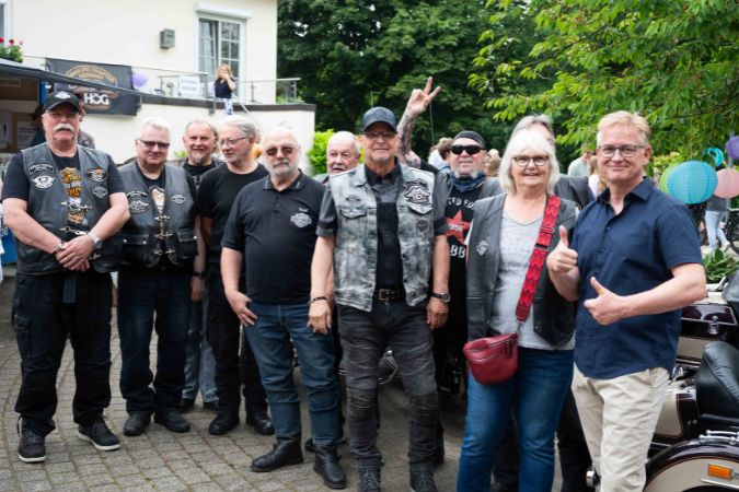 Eine Gruppe von Motorradfahrern posiert für ein Foto, einige tragen Lederjacken und Sonnenbrillen.