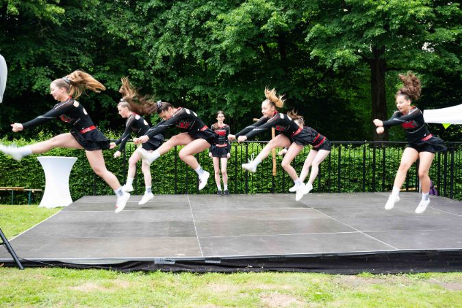 Gruppe von Cheerleaderinnen, die synchron auf einer Bühne springen und tanzen.