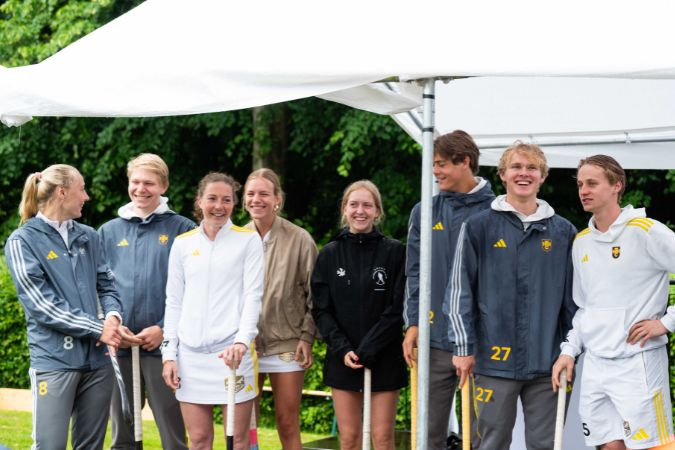 Eine Gruppe von acht Hockeyspieler:innen in Sportkleidung steht unter einem Zelt.