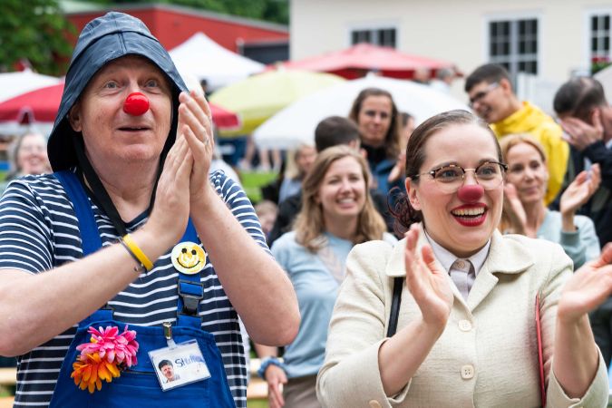 Zwei als Clowns verkleidete Personen applaudieren in einer Menschenmenge.