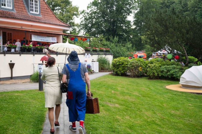 Zwei Personen gehen mit einem Regenschirm auf einem Weg in einem Garten.