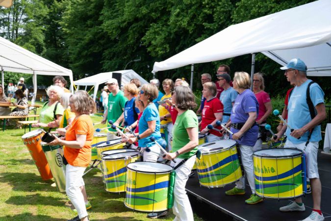 Eine Gruppe von Personen in bunten T-Shirts, die Trommeln bei einer Veranstaltung spielen.