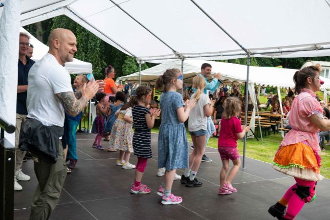 Gruppe von Kindern, die auf einer Bühne tanzen, begleitet von Erwachsenen.