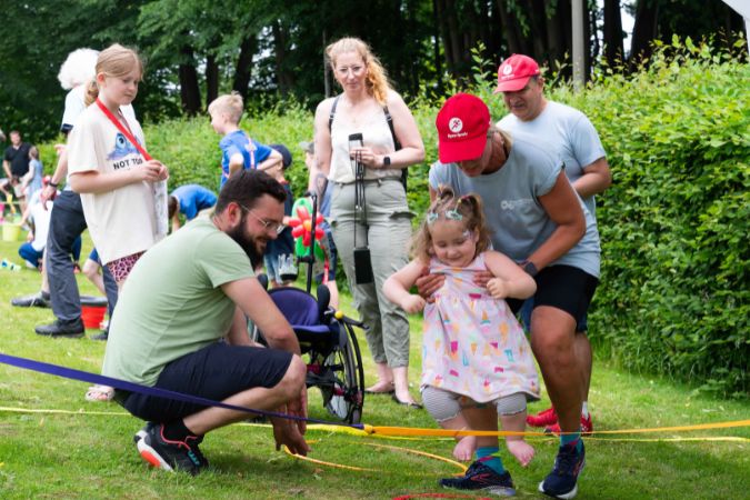 Ein Kind wird von zwei Erwachsenen beim Hüpfen über ein Seil unterstützt.