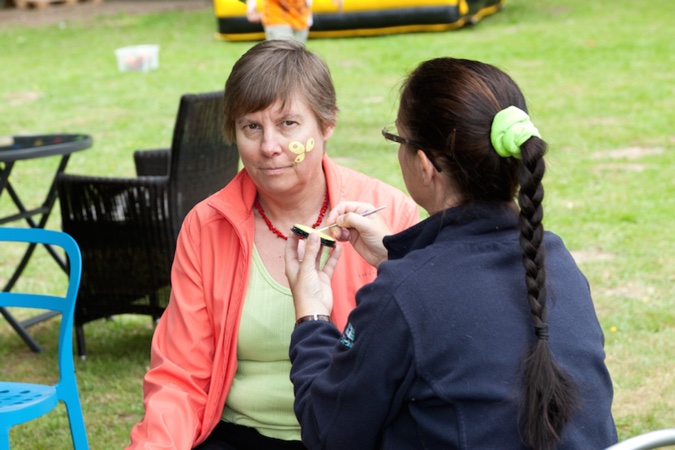 Eine Frau erhält Gesichtsbemalung mit gelben Punkten von einer anderen Frau im Freien.