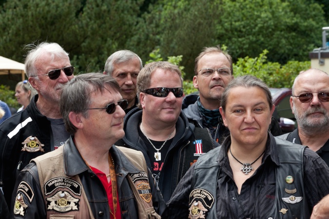 Eine Gruppe von Motorradfahrer:innen in Lederjacken steht zusammen und schaut in die Kamera.