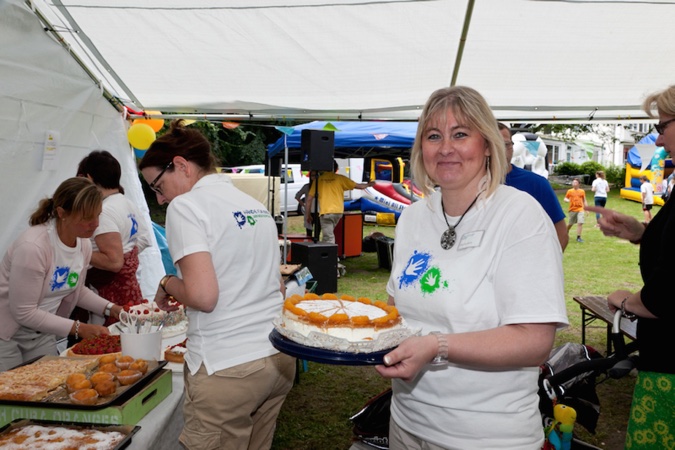 Eine Frau hält eine Torte, während andere Personen im Hintergrund am Kuchen-Buffet stehen.