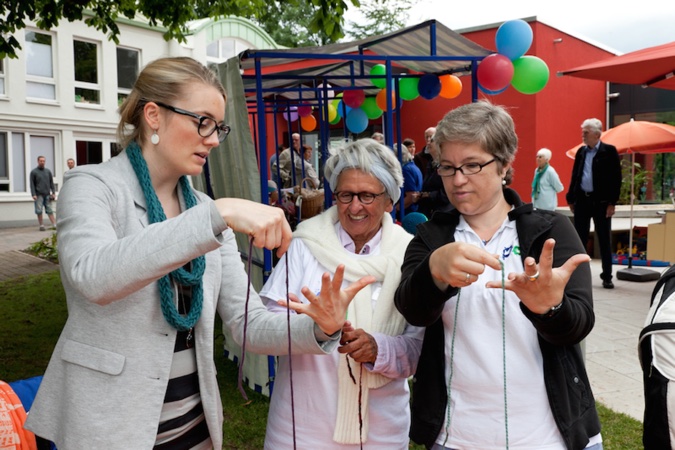 Eine Frau zeigt zwei weiteren Frauen, wie sie einen Faden um ihre Finger legen können.