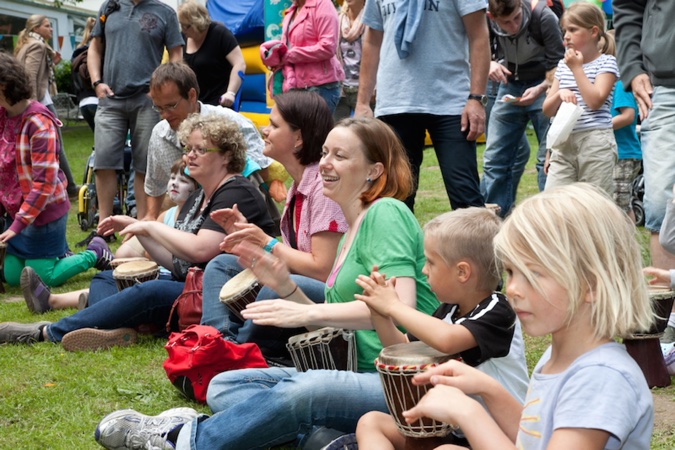 Gruppe von Menschen, die auf Trommeln spielen, einige sitzen auf dem Boden.