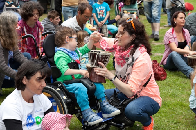 Ein Kind im Rollstuhl spielt mit einer Trommel, während eine Begleitperson hilft.