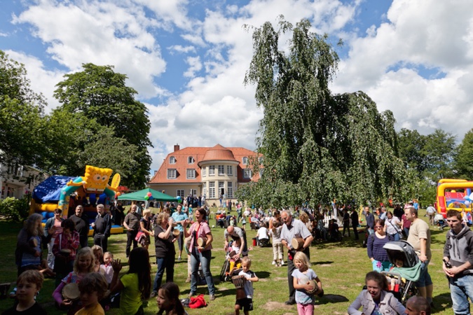 Eine Menschenmenge auf einem Sommerfest mit verschiedenen Aktivitäten im Hintergrund.