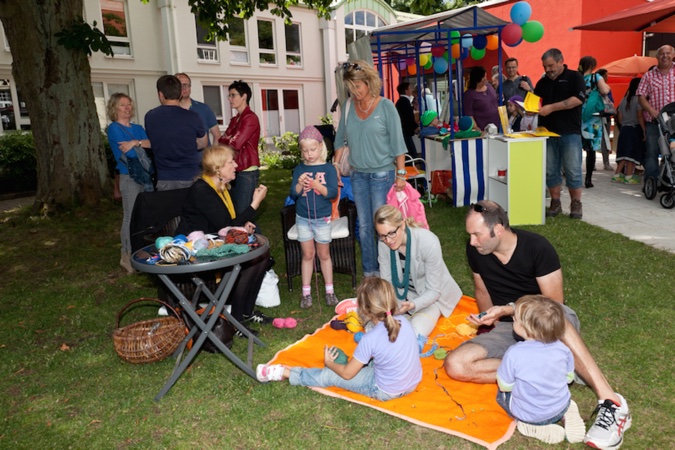 Gruppen von Menschen, die an einem Sommerfest im Freien teilnehmen, mit verschiedenen Aktivitäten und Ständen.