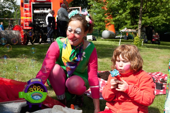 Clown mit buntem Kostüm und Kind, das mit einer Seifenblasenmaschine spielt.