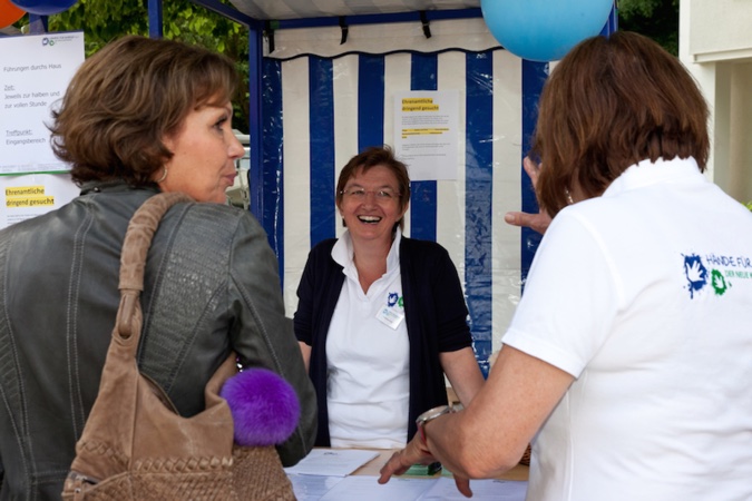 Mitarbeiterin an einem Stand auf einem Sommerfest, die mit zwei Frauen spricht.