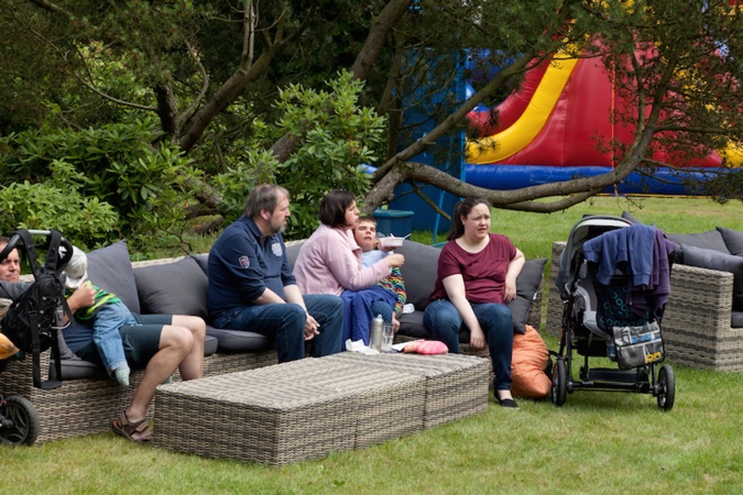 Eine Gruppe von Personen sitzt auf einer Couch im Freien, während ein aufblasbares Spielgerät im Hintergrund sichtbar ist.