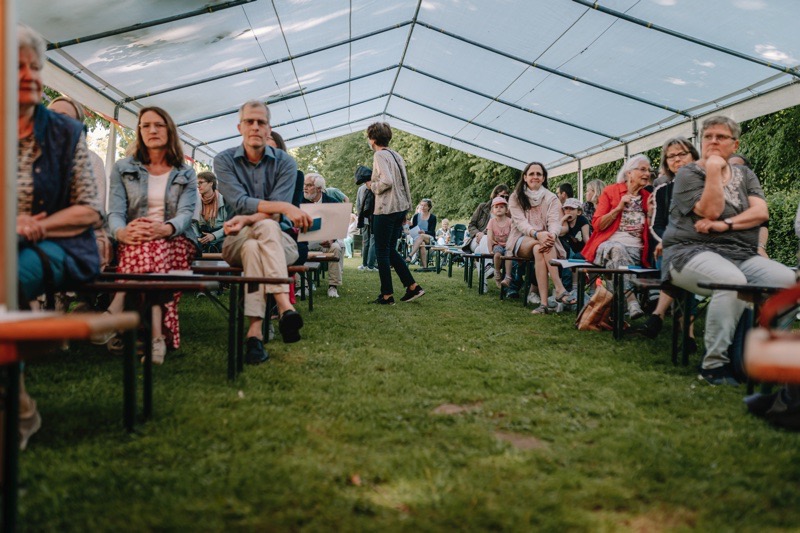 Gruppe von Menschen, die in einem Zelt auf Bänken sitzen.