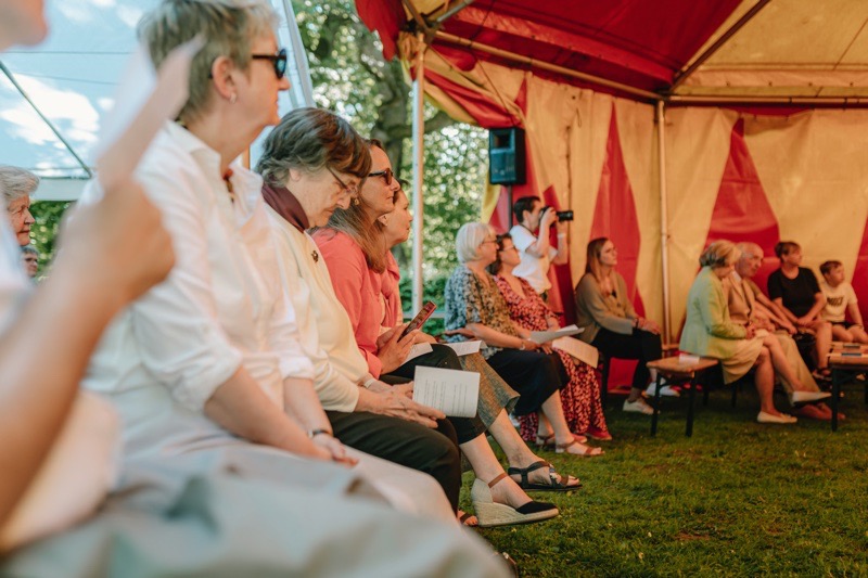 Gruppe von Personen, die in einem Zelt sitzen, einige halten Papier in der Hand.