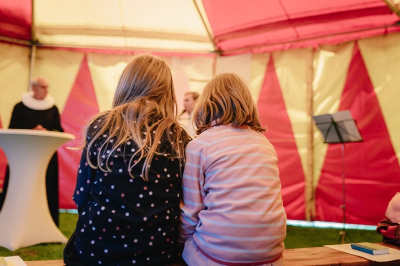Zwei Mädchen sitzen nebeneinander in einem Zelt mit bunten Wänden.