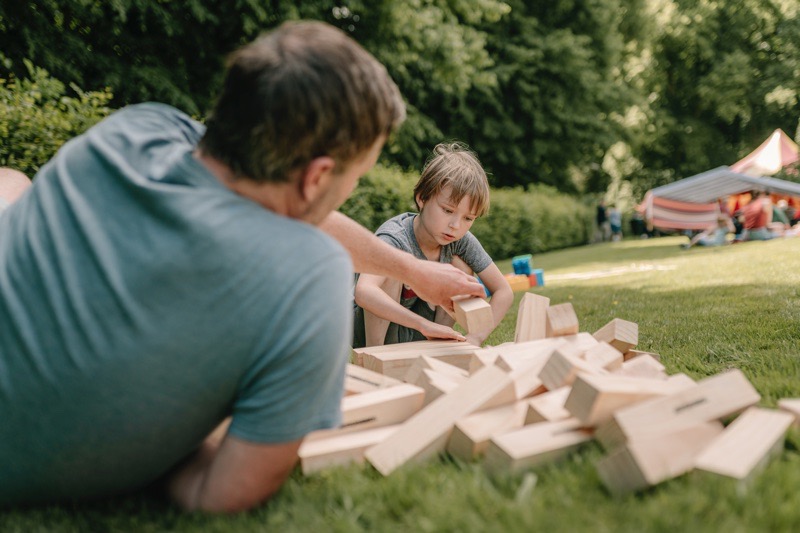 Ein Mann und ein Junge spielen mit großen Holzklötzen auf einer Wiese.